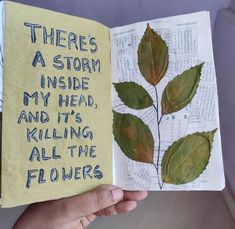 a hand holding an open book with writing on it and green leaves in the pages