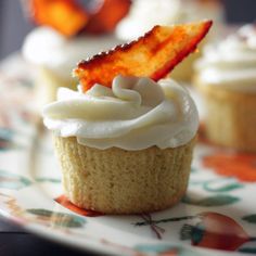 some cupcakes with white frosting and a slice of bacon on top are sitting on a plate