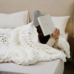 a woman laying in bed under a white blanket with a book on top of her head