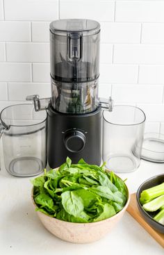 a bowl filled with green vegetables next to a food processor and other kitchen gadgets