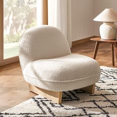 a white chair sitting on top of a wooden floor next to a lamp and rug