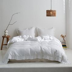 a bed with white linens and pillows in a minimalistic bedroom setting, including a lamp