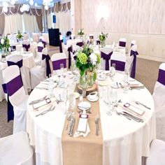 a banquet room set up with white and purple linens, silverware and flowers