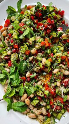 a white plate topped with lots of vegetables and beans next to a spoon on top of a table