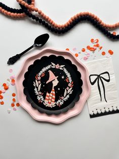 a pink and black plate sitting on top of a table next to some beads, spoons and other items