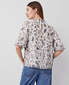 Elevate your wardrobe with the Ann Taylor Paisley Clip Ruffle Split Neck Popover Top, a piece that blends sophistication with comfort. This top features a charming ruffle split neck and is delicately shirred for added texture. The short sleeves boast shirred caps and elasticized cuffs, enhancing its elegant silhouette.

- Size: XL
- Color: Winter White-Baguette
- Material: Shell: 95% Polyester, 5% Other Fiber; Lining: 100% Polyester
- Gender: Female
- Fit: Blousy - a relaxed, flowing fit
- Lengt Casual Blouse With Blouson Sleeves And Tie Neck, Casual Tops With Blouson Sleeves And Tie Neck, Paisley Print Tops For Workwear In Summer, Casual Tie Neck Peasant Top For Fall, Casual Fall Peasant Top With Tie Neck, Casual Paisley Print Top For Workwear, Blouson Sleeve, Blouse Tops, Petite Tops