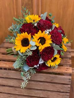 a bouquet of sunflowers and red roses on a wooden crate