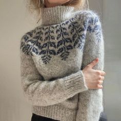 a woman wearing a gray sweater with blue and white designs on it