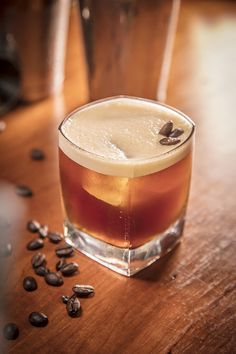 a glass filled with liquid sitting on top of a wooden table next to coffee beans