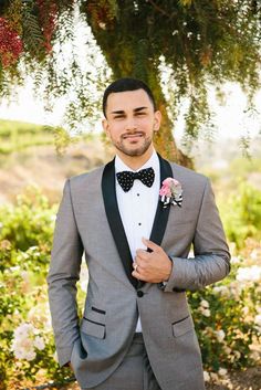 a man in a tuxedo and bow tie standing under a tree with flowers