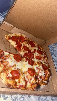 a pepperoni pizza sitting inside of a box on a bed with blue and white bedspread