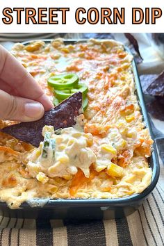 a hand dipping a tortilla chip into a casserole dish with cheese and vegetables