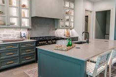 a kitchen with blue cabinets and white counter tops, an island in the middle has bottles on it