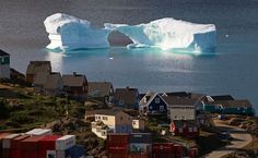 an iceberg floating in the ocean next to small houses and buildings with snow on them