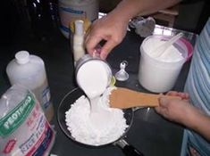 two people are mixing ingredients in a bowl on a counter top, one is pouring milk and the other is using a wooden spoon