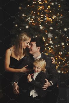 a man and woman are hugging their son in front of a christmas tree with lights