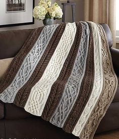 a brown and white blanket sitting on top of a couch next to a vase with flowers