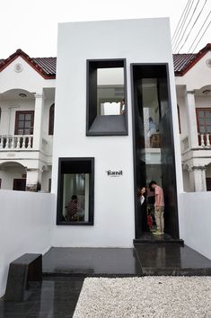 two people standing in the doorway of a small white house with black trim and windows