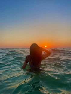 a woman sitting on top of a surfboard in the middle of the ocean at sunset