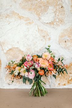 a bouquet of flowers sitting on top of a table next to a stone wall in front of it