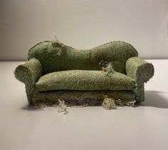 an old green couch is covered with moss and lace, sitting on a white surface