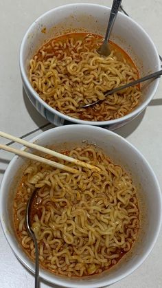 two bowls filled with noodles and chopsticks on top of a white countertop