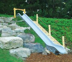 a slide is in the middle of a rock wall and green grass on the other side