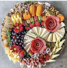 a platter filled with cheeses, fruits and flowers on top of a table