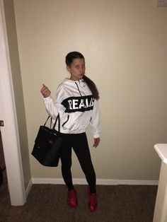 a woman standing in a room holding a black purse and wearing a white sweatshirt with the word team on it