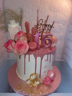 a birthday cake decorated with pink and white icing, gold decorations and flowers on top