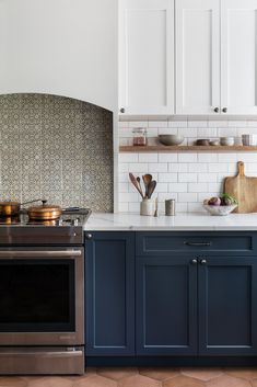 a kitchen with blue cabinets and stainless steel stove top oven in the center, surrounded by white subway backsplash tiles