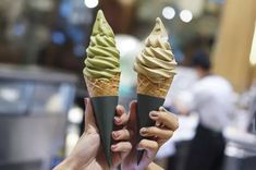 two ice cream cones are being held up in front of the camera with their hands