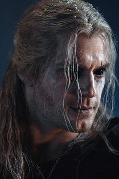 a man with long hair wearing a black shirt and silver chain necklace, staring at the camera