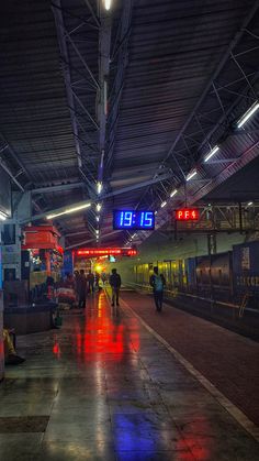 people are walking in the rain at a train station as it is raining with red, blue and green lights