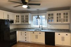 an empty kitchen with black appliances and white cupboards on the counter top, along with a ceiling fan