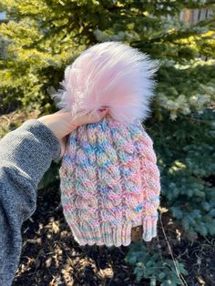 a person holding up a pink and blue knitted hat with fuzzy pom - pom