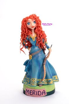 a doll with red hair and blue dress holding a bow on top of a table