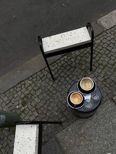 three cups of coffee sitting on top of a black table next to a white bench