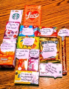 many different types of candy on a wooden table with notes attached to them and some writing on the bags