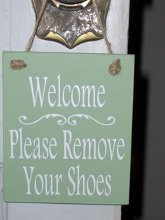 a welcome sign hanging from the side of a white door that says, welcome please remove your shoes