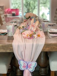 the table is set with pink napkins and flowers on it, along with butterfly decorations