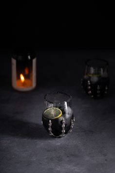 two small glass vases with lemon slices in them on a dark surface next to a lit candle