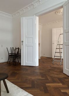 an empty room with wooden floors and white walls, has a ladder leading to the door