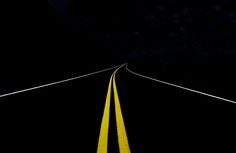 an empty road in the dark with yellow lines going down one side and another way to the right