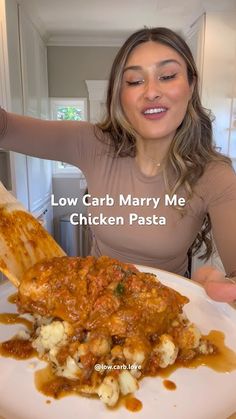 a woman holding a wooden spoon in front of a plate of food that has chicken and gravy on it