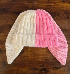 a pink and white knitted hat sitting on top of a wooden table