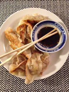 a white plate topped with dumplings and chopsticks on top of a table