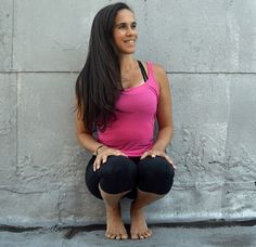 a woman sitting on the ground with her hands in her pockets and smiling at the camera