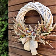 a white wreath hanging on the side of a wooden wall next to a bushy plant