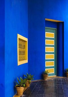 a blue building with potted plants in front of it and a yellow door on the side